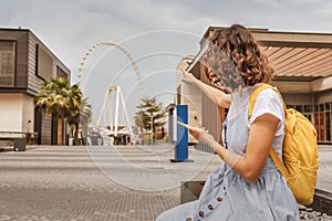 Woman with smartphone pointing at the largest Ferris wheel in the world - Dubai Eye. Top tourist attractions and sightseeing in