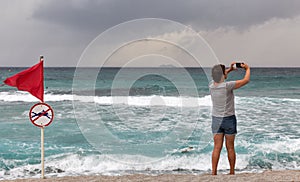 Woman with smartphone and red warning flag on sea beach