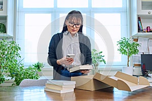 Woman with smartphone unpacking box with books, online shopping