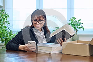 Woman with smartphone unpacking box with books, online shopping