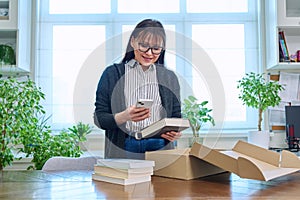 Woman with smartphone unpacking box with books, online shopping