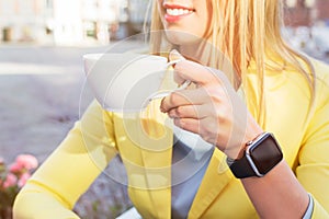 Woman with a smartwatch around her wrist holding a cup of coffee