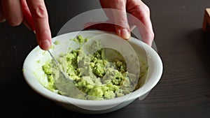 woman smashing avocado in white bowl