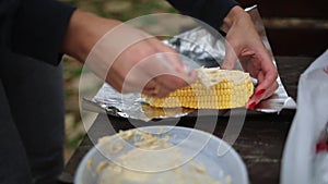 A woman smears corn with oil and spices to bake in foil over a fire. Hands and corn close-up