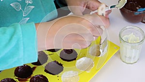 A woman smears a silicone mold to make candies glazed with chocolate with melted white chocolate. Nearby is almonds for the fillin