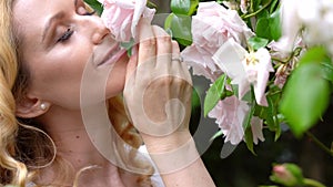 Woman smelling and enjoying beautiful roses flowers beautiful sunny spring day. Smiling young woman posing with blossom  flowers h