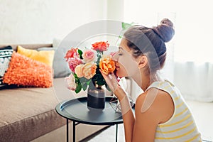 Woman smelling fresh roses in vase on table. Housewife taking care of coziness in apartment. Interior and decor