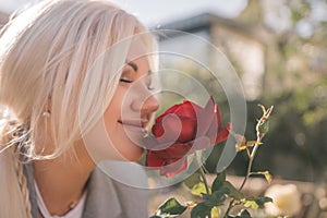 A woman is smelling a red rose. Concept of happiness and contentment, as the woman is enjoying the scent of the flower.