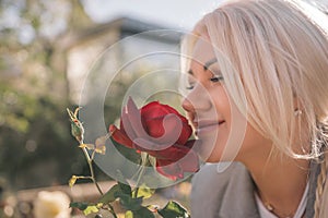 A woman is smelling a red rose. Concept of happiness and contentment, as the woman is enjoying the scent of the flower.