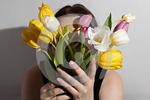 A woman smells colorful tulips in her hands in a room illuminated by sunlight