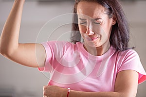 Woman smells herself with repulsive facial expression and sweat patches on her pink shirt