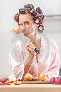 Woman smells onion and frowns while holding it stick to a knife in her hand