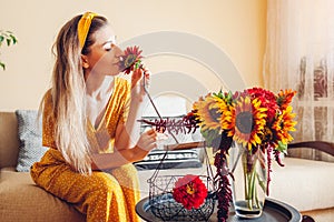 Woman smells sunflower arranging bouquet with zinnia flowers in vase at home. Lady enjoys fresh blooms. Interior