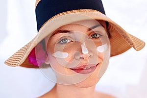 Woman smile applying sun cream  on face. Skincare. Body Sun protection. sunscreen. Female in hat smear  moisturizing lotion on ski