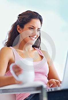 Woman, smile and coffee with laptop with reading digital blog and relax wellness in chair in home. Young person, happy