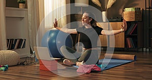 A woman with a smile greets her charges at an online training session waving at a laptop camera. Athletic trainer begins