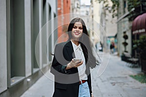 Woman smile with teeth with a phone in her hands walks around the city fashion on the street, spring travel, vacation in