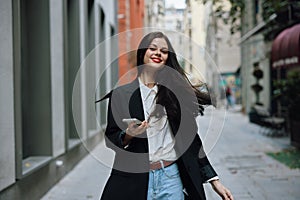 Woman smile with teeth with a phone in her hands walks around the city fashion on the street, spring travel, vacation in