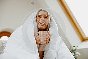 The woman smiles happily while wrapped in a blanket, holding a cup of coffee