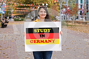 A woman smiles and holds a poster with the text Study in Germany