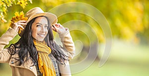 Woman smiles outdoors on a fall day wearing hat, jacket and a scarf, all in yellow and beige color tones