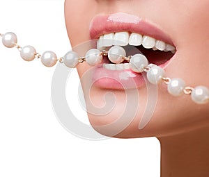 Woman smiles showing white teeth, holding a pearly necklace into the mouth