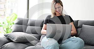 Woman smiles, sits on sofa participates in remote webinar