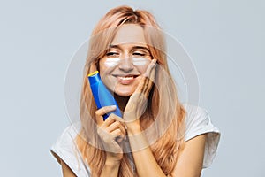 Woman smiling and applying suntan cream sunscreen lotion on face, cheeks with sun protection cream. Sunburn