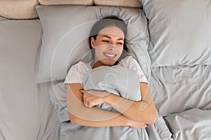 Woman smiling in bed, hugging pillow, happy morning