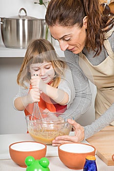 Woman and smiling child whipping to make a cake