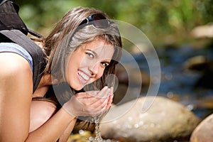 Woman smiling and drinking water with hands from stream
