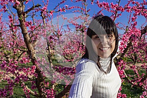 Woman smiling among fields of blooming peach trees in spring