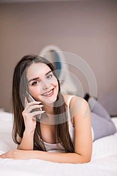 Woman smiling with her mobile phone on bed talking and texting at home