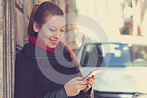 Woman smiling holding a mobile phone standing outdoors next to new car