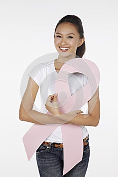 Woman smiling while hugging a pink breast cancer ribbon. Conceptual image