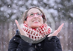 Woman smiling joyfully with hands up as winter snow falls down,