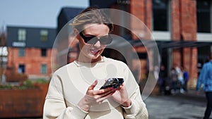 Woman smiling and looking ahead while holding modern gadget in hands outdoors