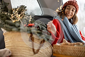 Woman smiling and looking at sparkler while sitting in car trunk