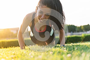 Woman smiling while is making plank on the grass of a park in the morning