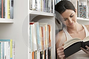 Woman Smiling While Reading By Bookshelves photo