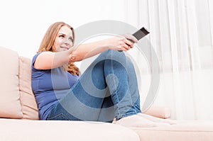 Woman smiling relaxing on sofa holding remote control