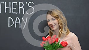 Woman smiling and smelling tulips, happy mothers day on blackboard, congratulate