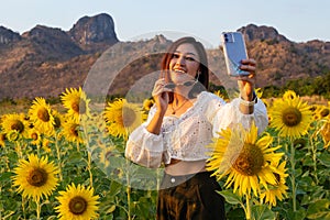 Woman smiling while taking selfie picture with mobile phone in sunflower field at Kao Jeen Lae in Lopburi, Thailand