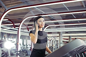 Woman smiling while talking on mobile phone while running on treadmill