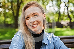 Woman smiling toothy to the camera while sitting at the bench in good mood