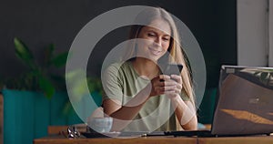 Woman smiling while typing on phone in a coffeeshop.Woman surfing the internet and contacting people