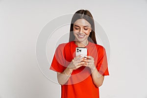 Woman smiling while using mobile phone isolated over white wall