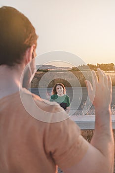 Woman smiling and waving at a friend in the nature at sunset