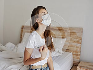 Woman snake qing mask sitting on the bed checking the temperature with a thermometer