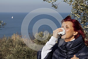 Woman sneezing, blowing nose into tissue above sea coast